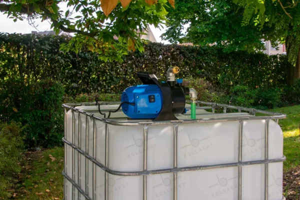 Gereinigde witte watertank van 1000 liter met gegalvaniseerde kooi, pomp, aftapkraan en metaal of kunststofen onderstel. linkeraanzicht-vooraanzicht-in-tuinomgeving