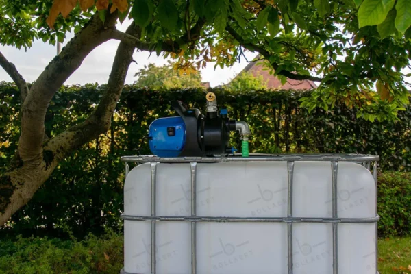 Gereinigde witte watertank van 1000 liter met gegalvaniseerde kooi, pomp, aftapkraan en metaal of kunststofen onderstel. vooraanzicht-in-tuinomgeving