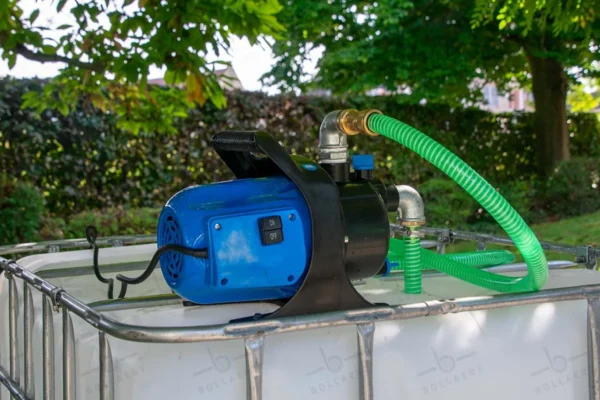 Gereinigde witte watertank van 1000 liter met gegalvaniseerde kooi, pomp, aftapkraan en metaal of kunststofen onderstel. zijaanzicht-pomp-met-uitgaande-slang